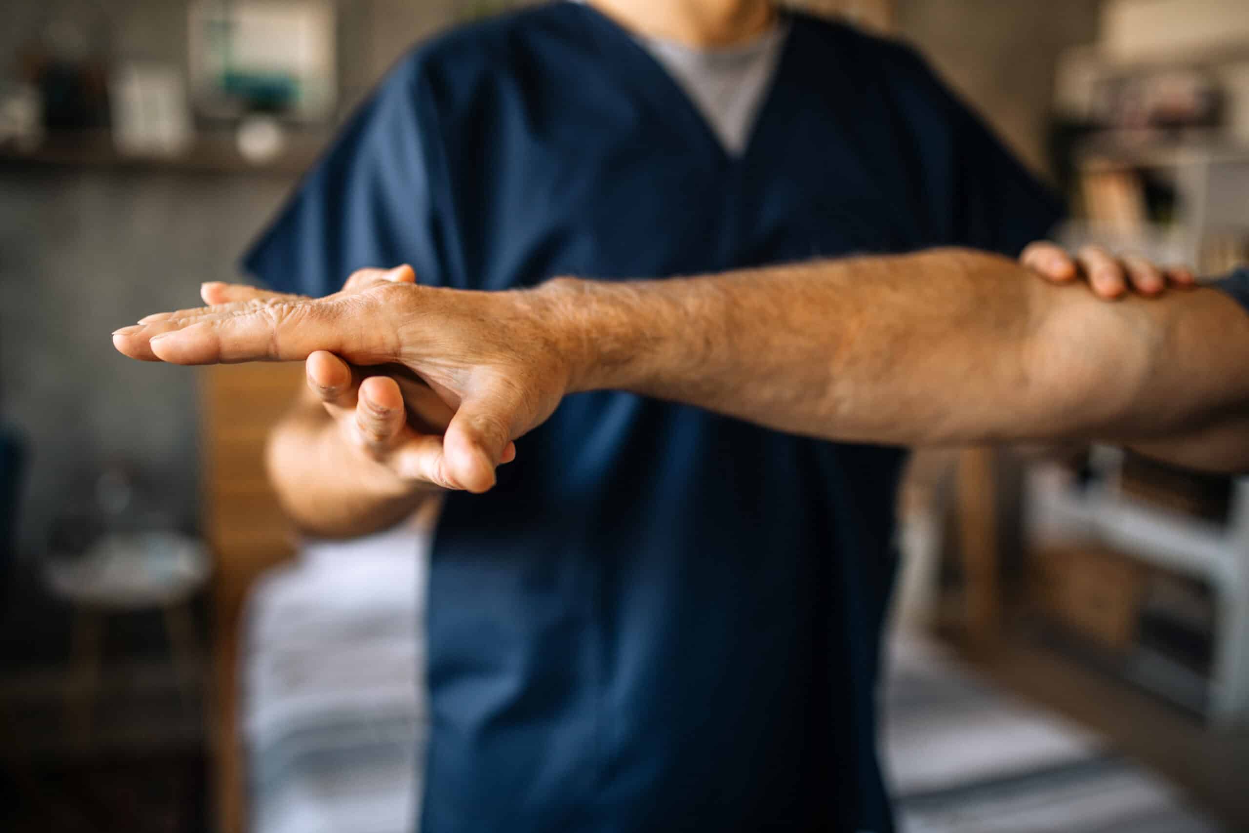 Giovane fisioterapista aiuta paziente più anziano a svolgere esercizi di riabilitazione al braccio a domicilio a Torino